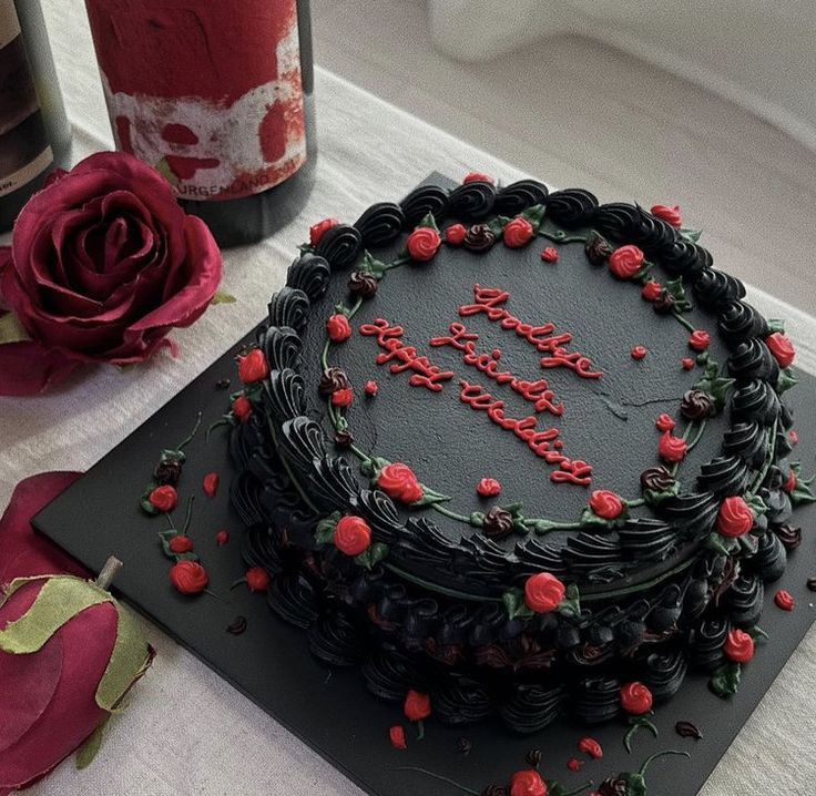 a black cake with red roses on it and a bottle of wine in the background