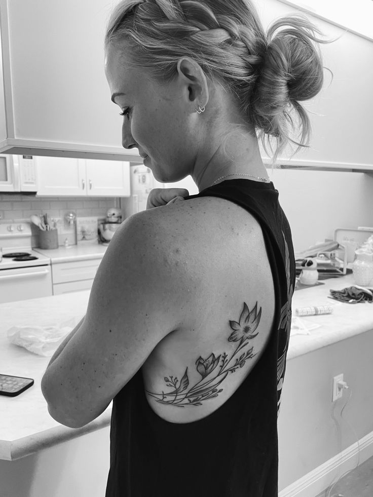 a woman with a flower tattoo on her upper arm and shoulder, standing in a kitchen