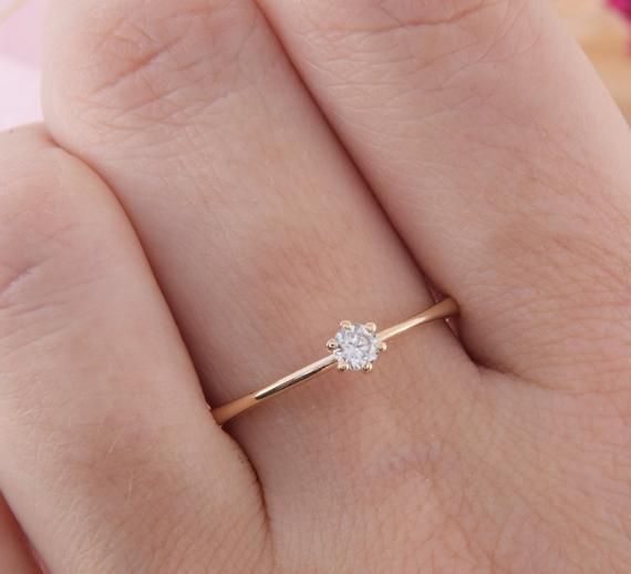 a woman's hand with a diamond ring on top of her finger and pink flowers in the background