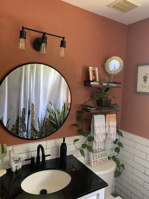 a bathroom with a black counter top and white tiles on the walls, along with a round mirror