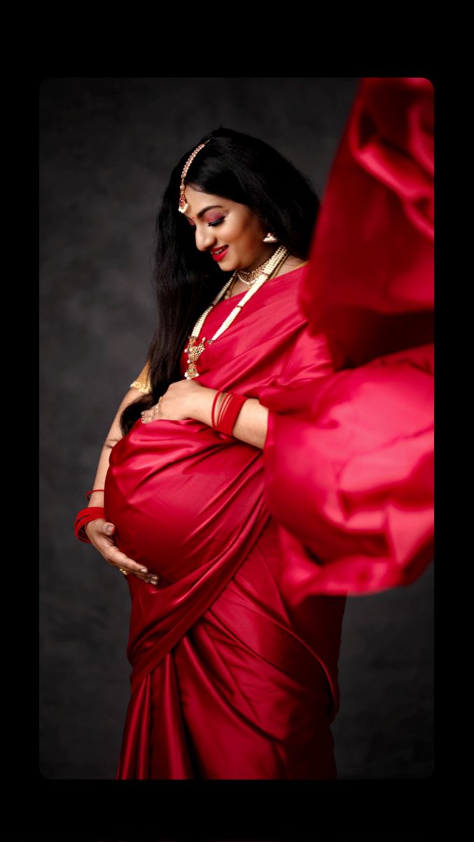 a pregnant woman in a red sari poses for the camera with her hands on her belly