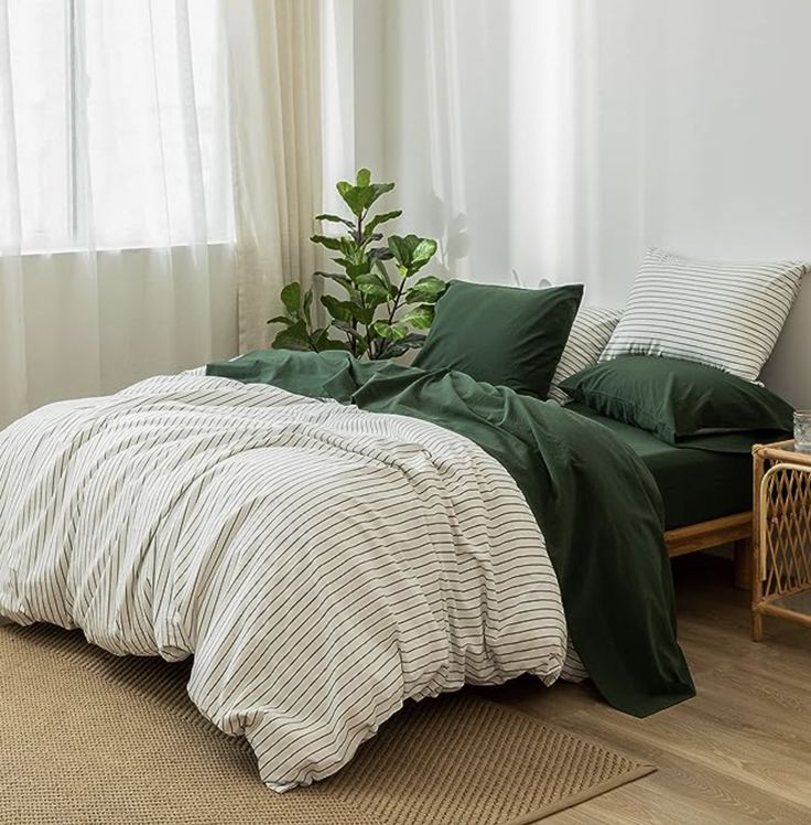 a bed with green sheets and pillows in a white room next to a potted plant