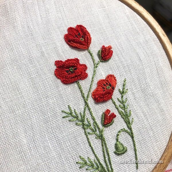 some red flowers are in the middle of a white embroidery pattern on a wooden hoop