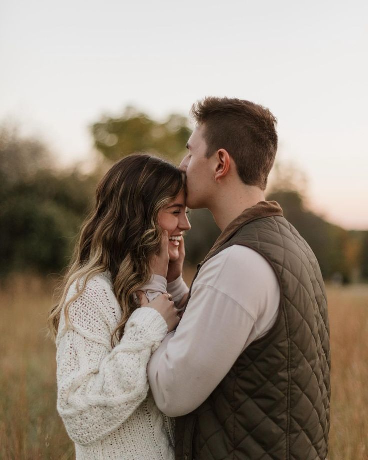 a man and woman standing in the middle of a field with their heads close to each other