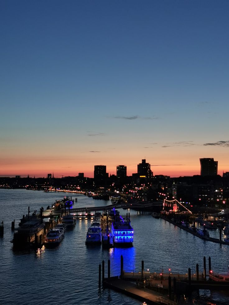 boats are docked in the water at dusk with city lights and buildings in the background