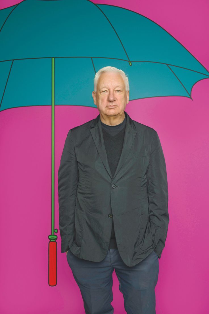 an older man standing in front of a colorful wall with an umbrella over his head