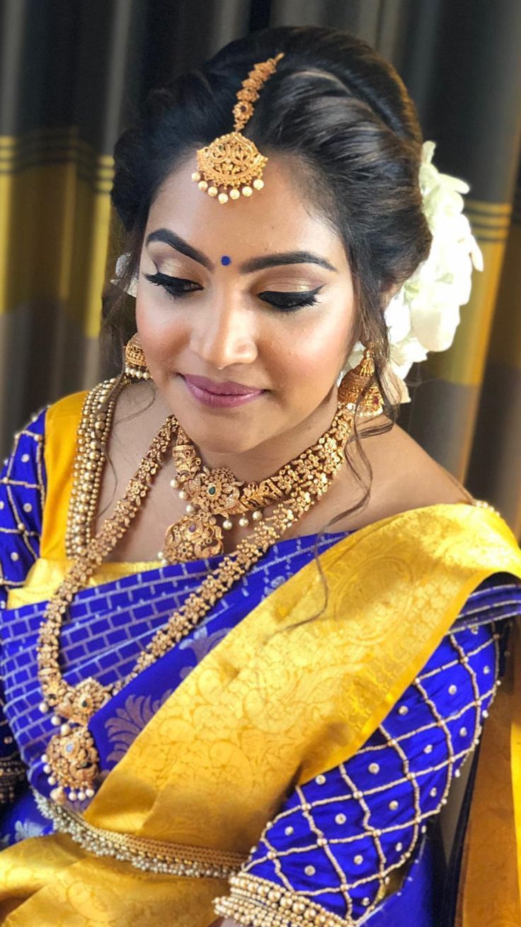 a woman in a blue and yellow sari with gold jewelry on her head, looking down