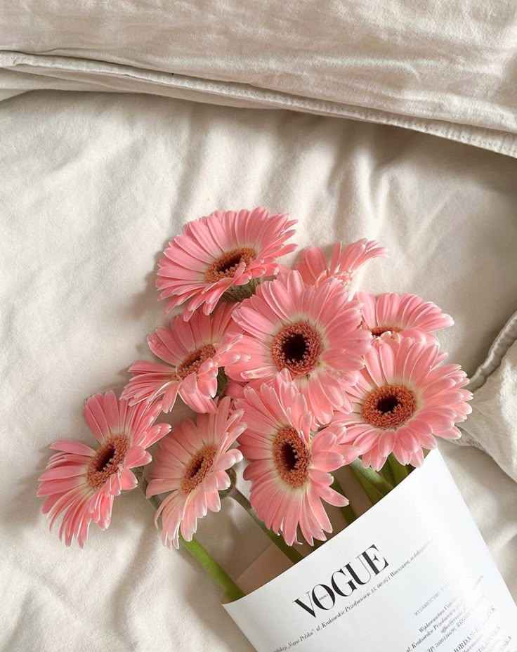 pink flowers are in a vase on a white sheet with an open book next to it