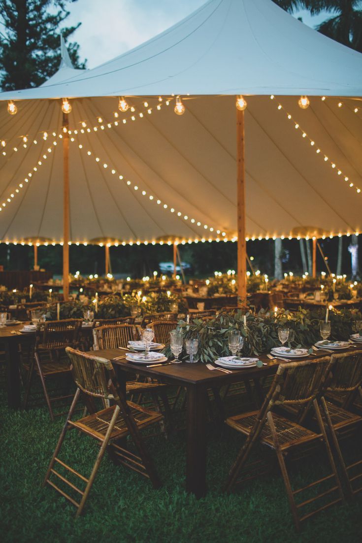 an outdoor tent with tables and chairs set up for dinner under string lights at night