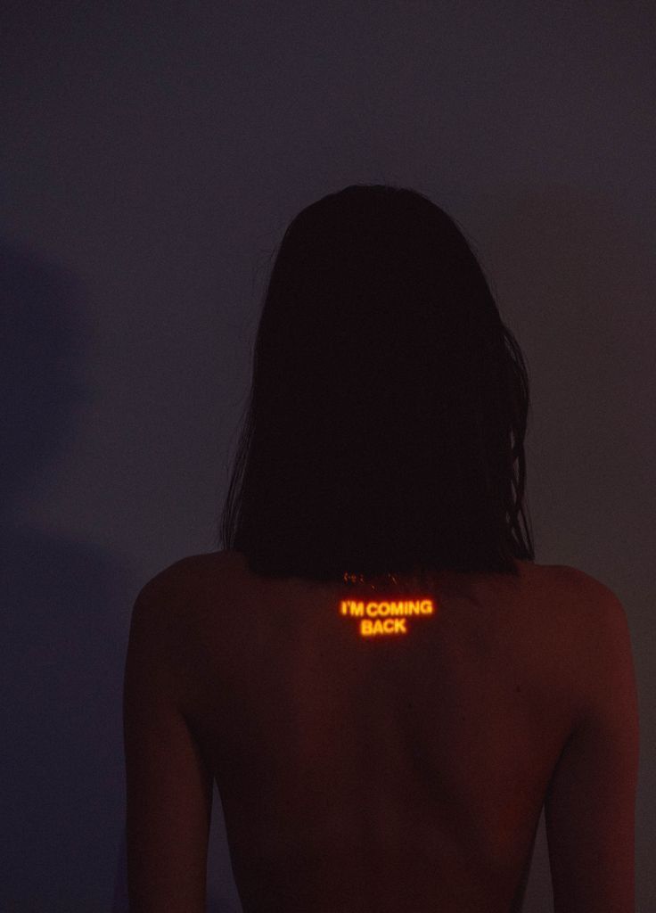 the back of a woman's body with glowing words on it in yellow light