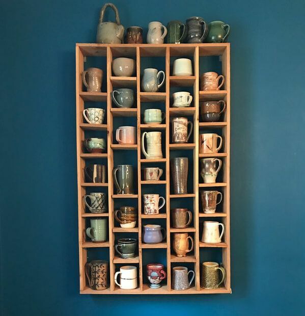 a wooden shelf filled with cups and mugs on top of a blue painted wall