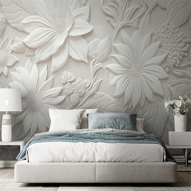 a large white bed sitting in front of a wall with flowers on it's headboard