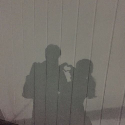 the shadow of two people standing next to each other on a white wall with wood slats