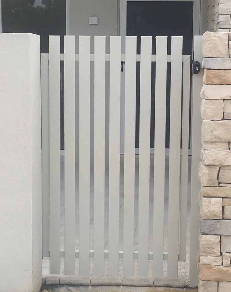 a cat sitting on the ground in front of a white gated entrance to a house