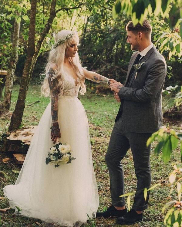 a bride and groom standing in the woods holding each other's hands as they look at each other