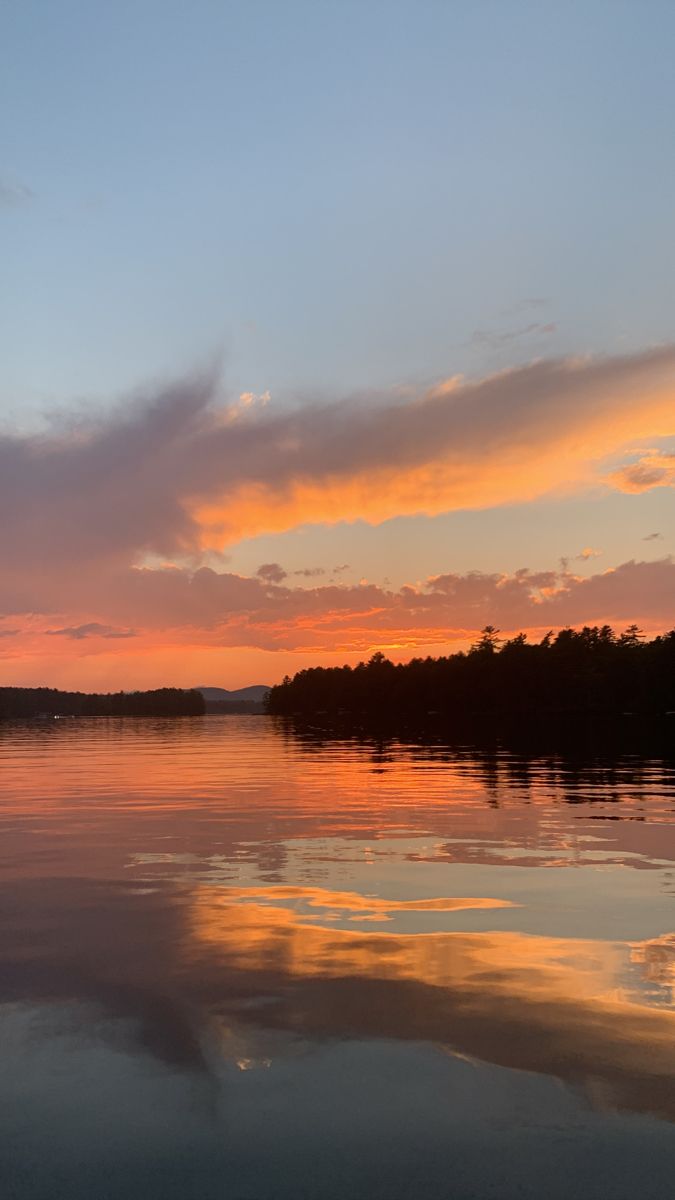 the sun is setting over some water with trees in the background and clouds reflected in the water