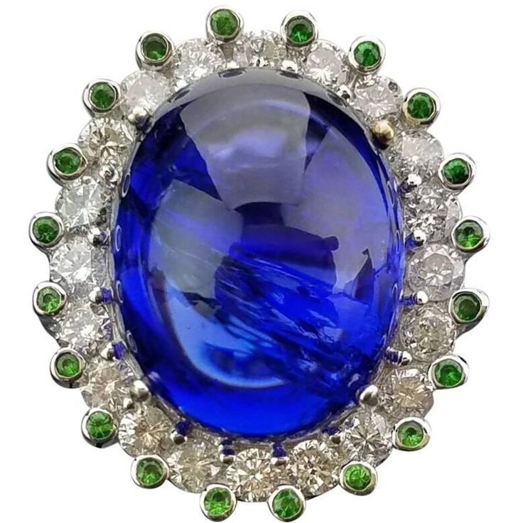 Statement Tanzanite cocktail ring, surrounded by a single Diamond tier and studded Green Garnet, mounted on 18K White Gold band. Stone Details: Stone: Tanzanite, Oval Cabochon, 19.78 carat Stone: Tsavorite, Round, 0.26 carat Diamond Details: Cut: Brilliant (round) Total Carat Weight: 1.46 Quality: VS/SI , H/I 18K Gold: 11.98 grams Can provide certificate upon request. Can change ring size upon request. Can provide cleaning/re-polish service (with extra charge) before shipping, upon request. Silver Halo Ring, Diamond Dress Ring, Yellow Gold Cocktail Ring, Garnet And Diamond Ring, Tanzanite Diamond Ring, Vintage Jewelry Art, Platinum Diamond Rings, Tsavorite Garnet, Tanzanite Diamond