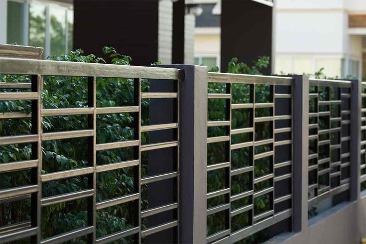 a metal fence with green plants growing on the top and bottom panels in front of it