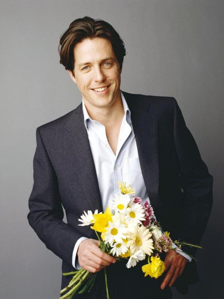 a man in a suit holding a bouquet of flowers and smiling at the camera with one hand on his hip