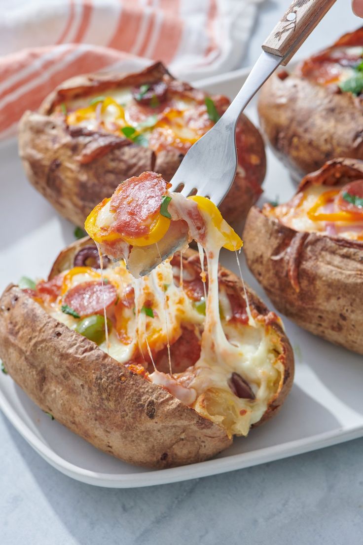 someone is cutting into some baked potatoes with cheese and pepperoni on them while they are sitting on a white plate