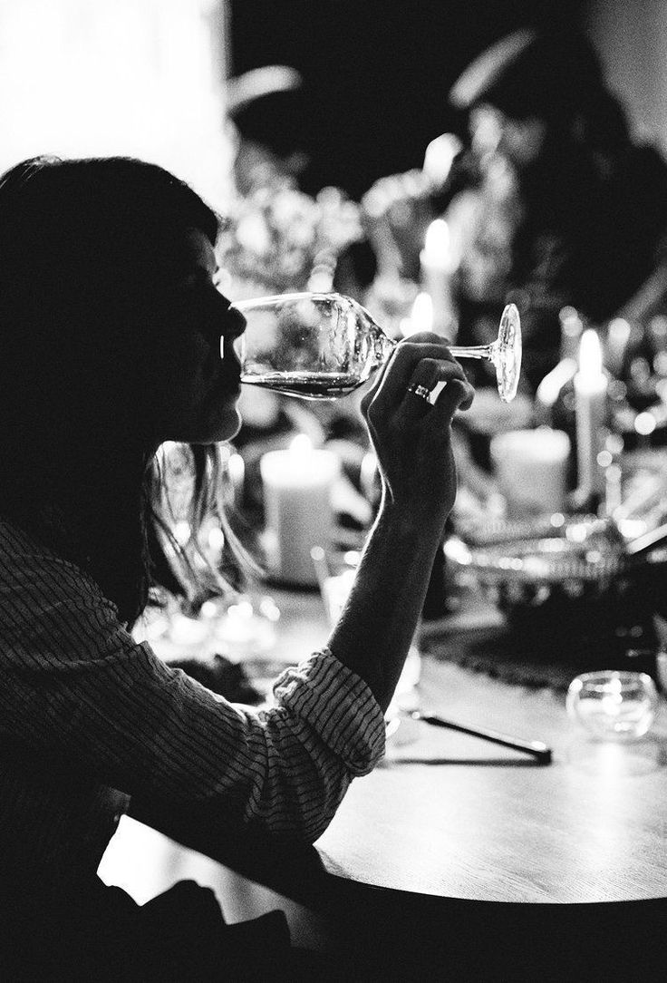 a woman sitting at a table drinking from a wine glass with candles in the background