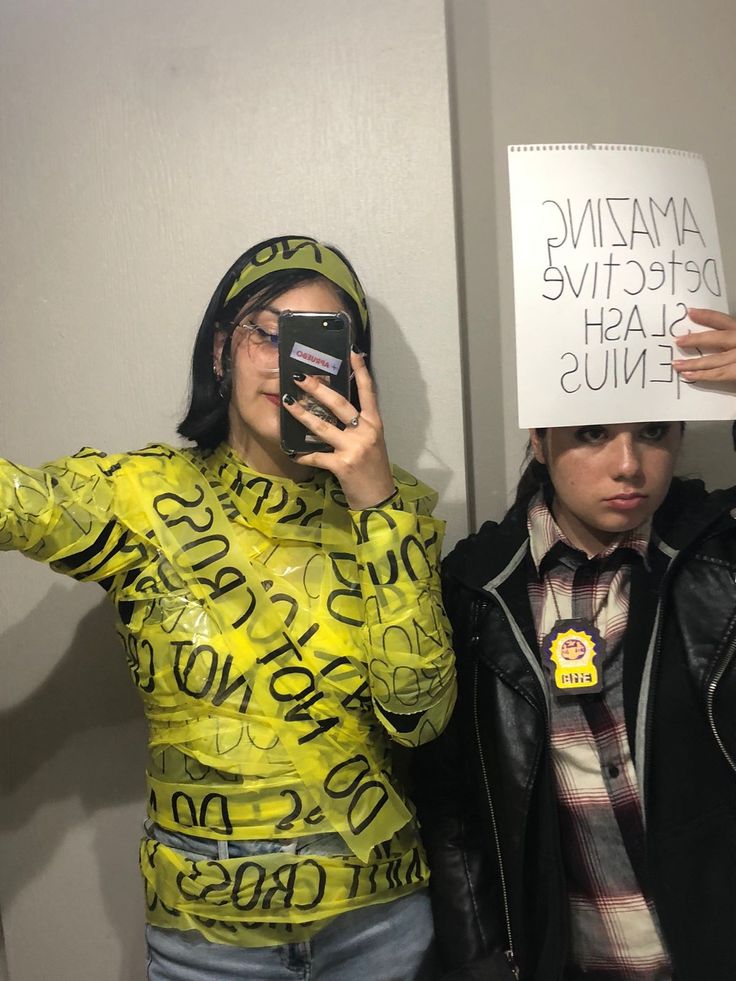 two people standing next to each other holding up cell phones and wearing yellow shirts with writing on them