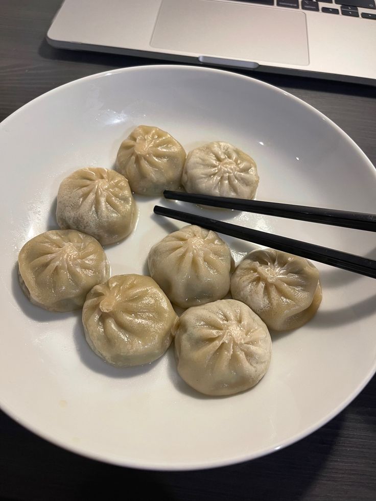 some dumplings and chopsticks on a white plate with a laptop in the background