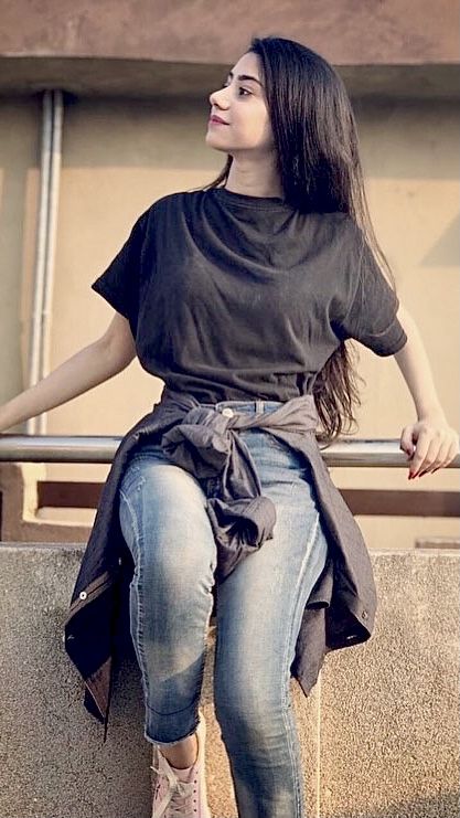 a woman sitting on top of a cement wall next to a metal rail and looking up at the sky