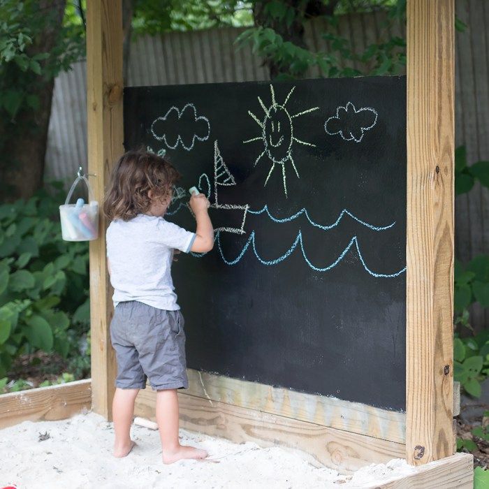 a little boy writing on a blackboard in the sand