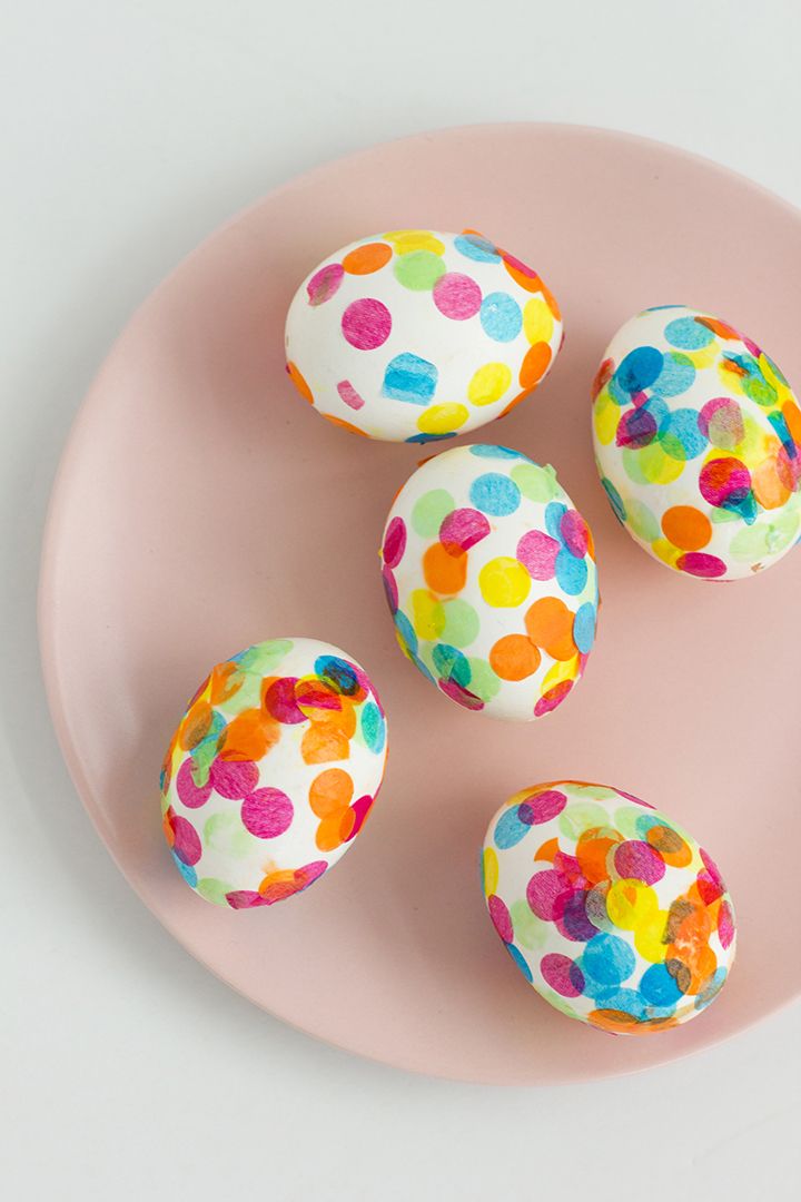 four decorated eggs on a pink plate with white and multicolored polka dot designs