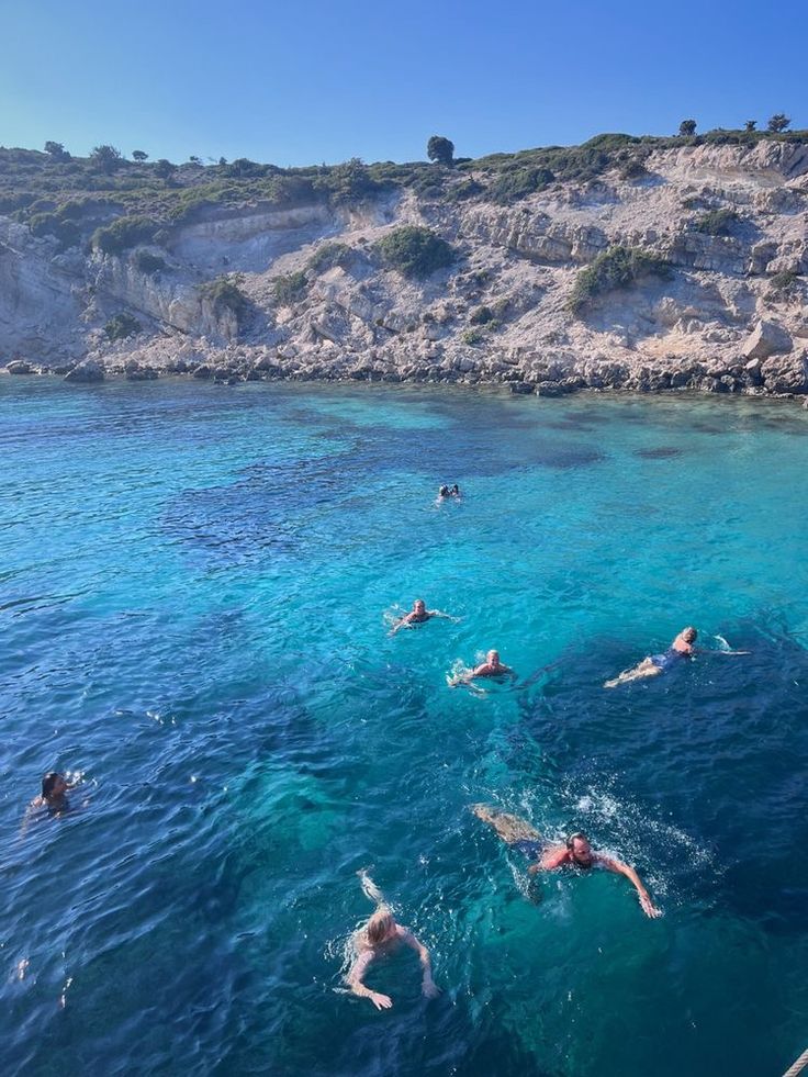 people swimming in the blue water near a rocky cliff and cliffs on top of it