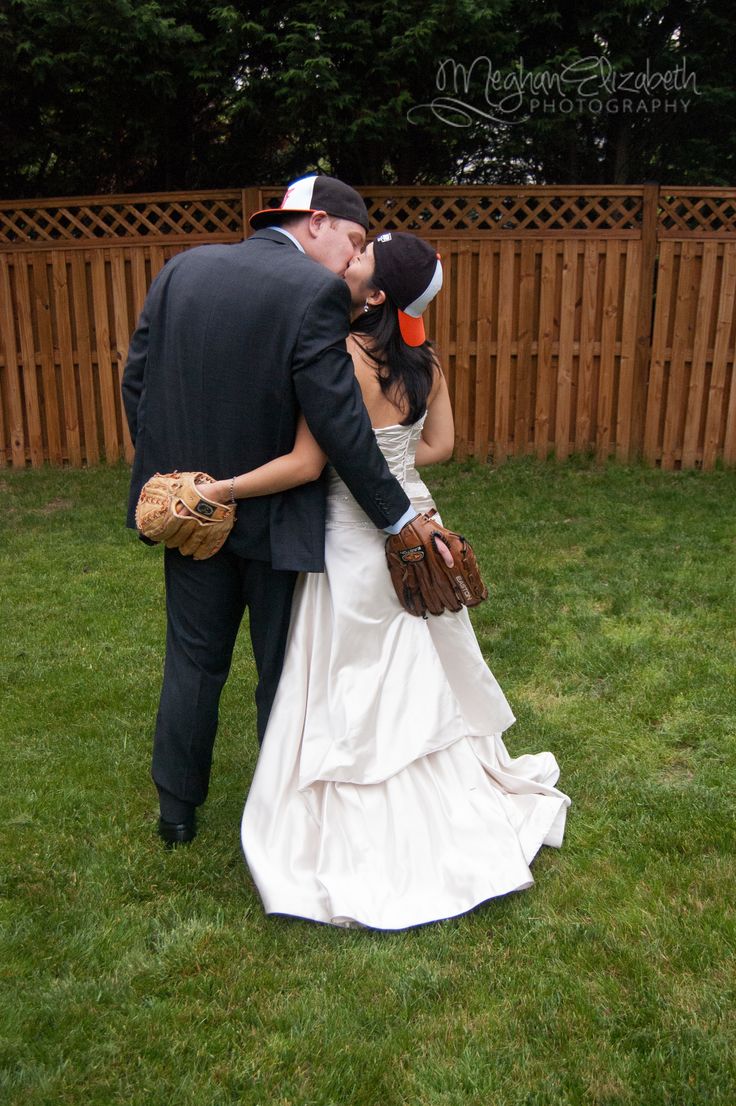 a bride and groom are kissing in the grass with baseball mitts on their hands