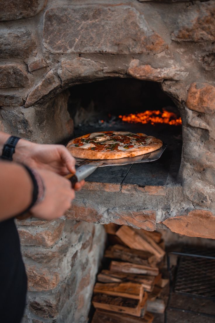 a person is holding a pizza in front of an open brick oven with wood logs