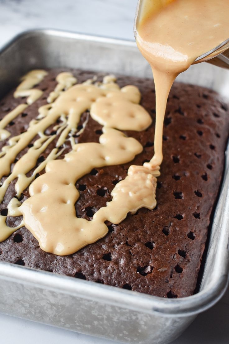 someone is spreading icing on top of a chocolate cake in a metal baking pan