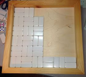 a wooden frame filled with white tiles on top of a table next to dices