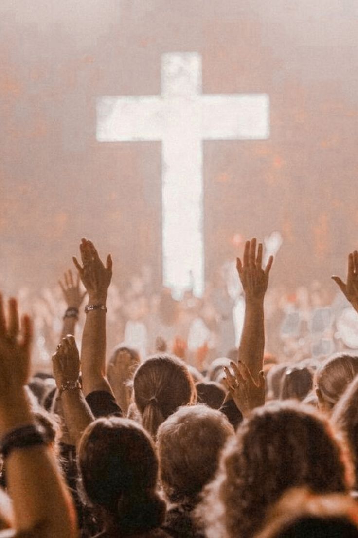 a large group of people raising their hands in front of a cross