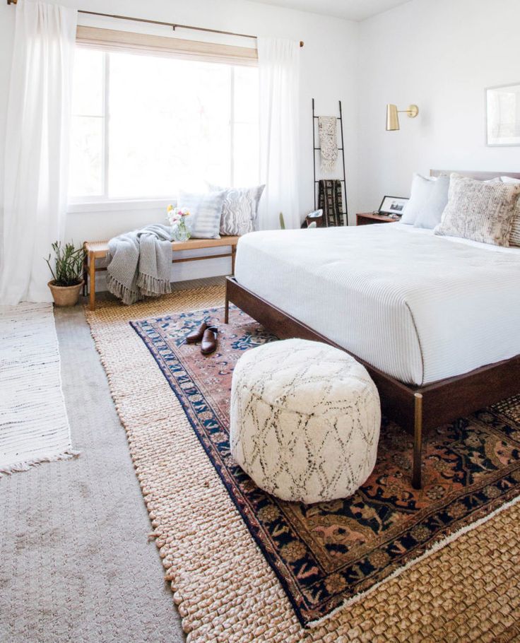 a bedroom with a large bed and rugs on the floor in front of a window