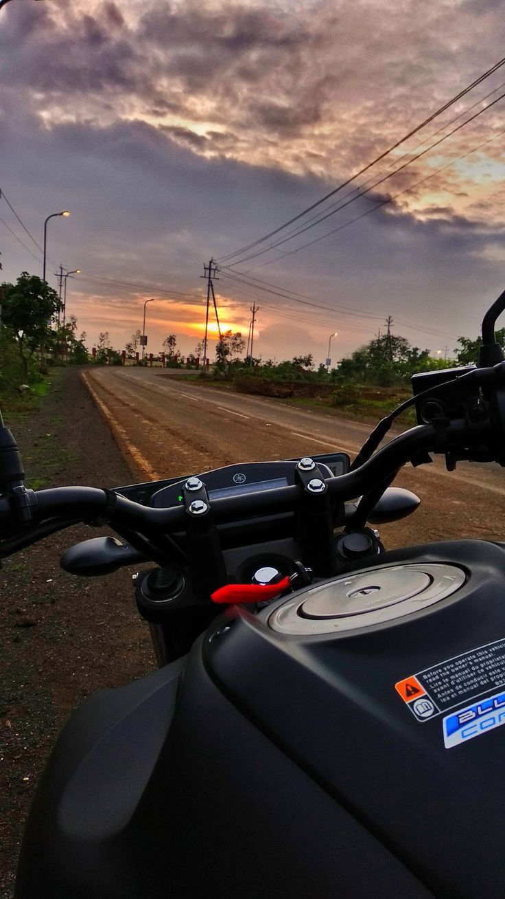 a motorcycle parked on the side of a dirt road under a cloudy sky with power lines in the distance