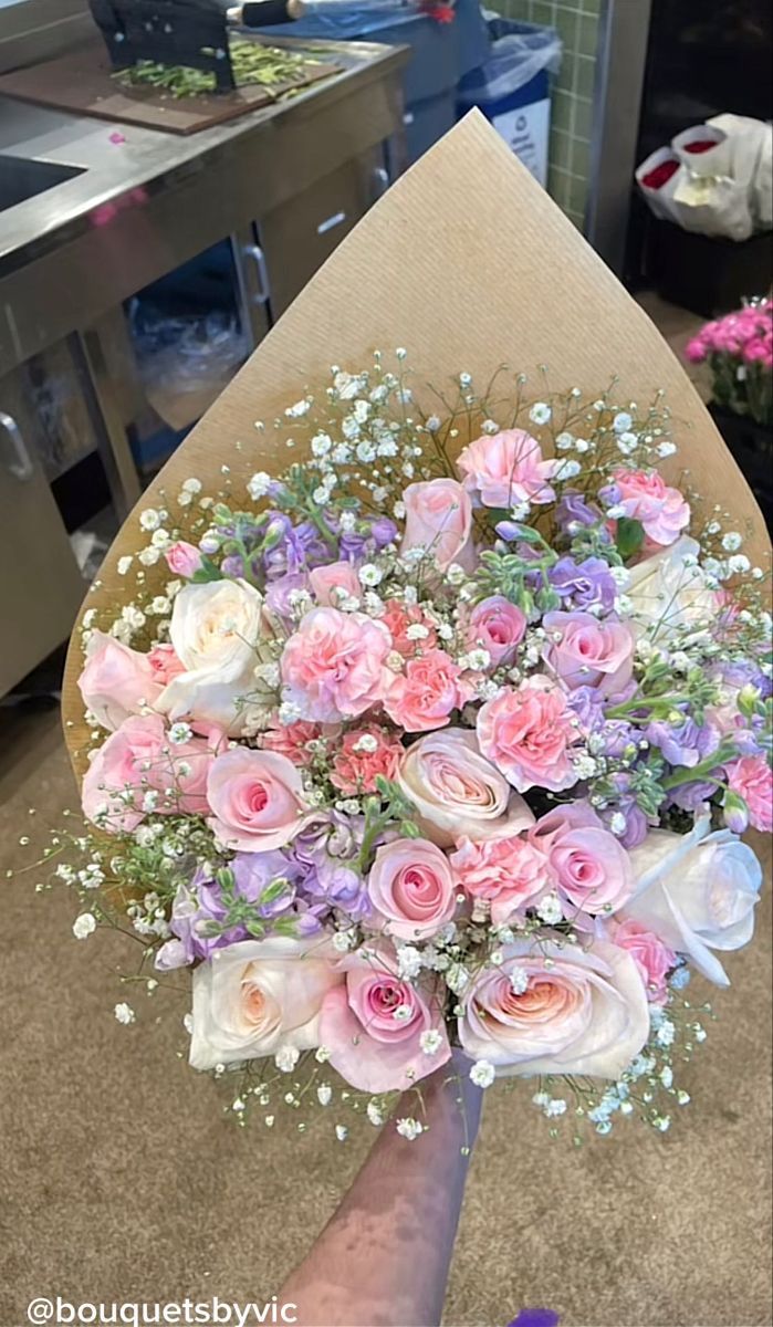 someone holding a bouquet of pink and white flowers in front of a kitchen counter top