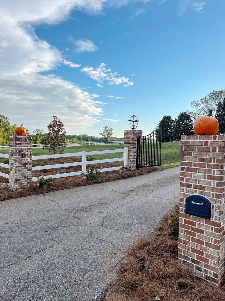 a brick gate with two pumpkins on top and a mailbox in the middle