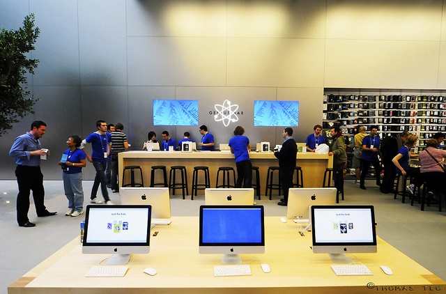 people are standing around in an apple store with computers on the tables and behind them is a display of books