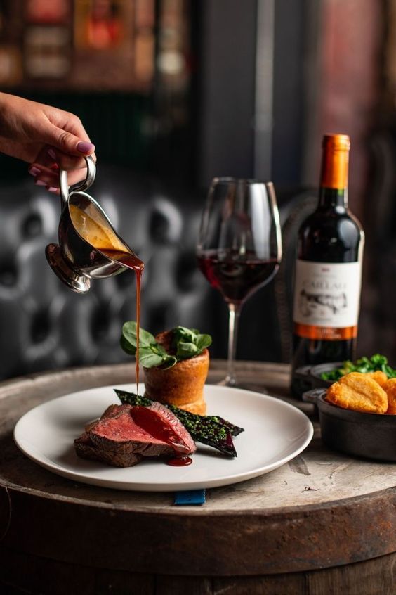 a person pours wine into a plate with meat and vegetables on the table next to it