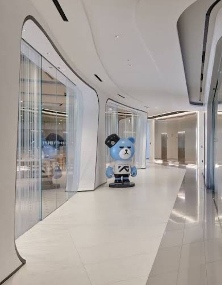 a blue teddy bear sitting in the middle of an empty room with glass walls and windows