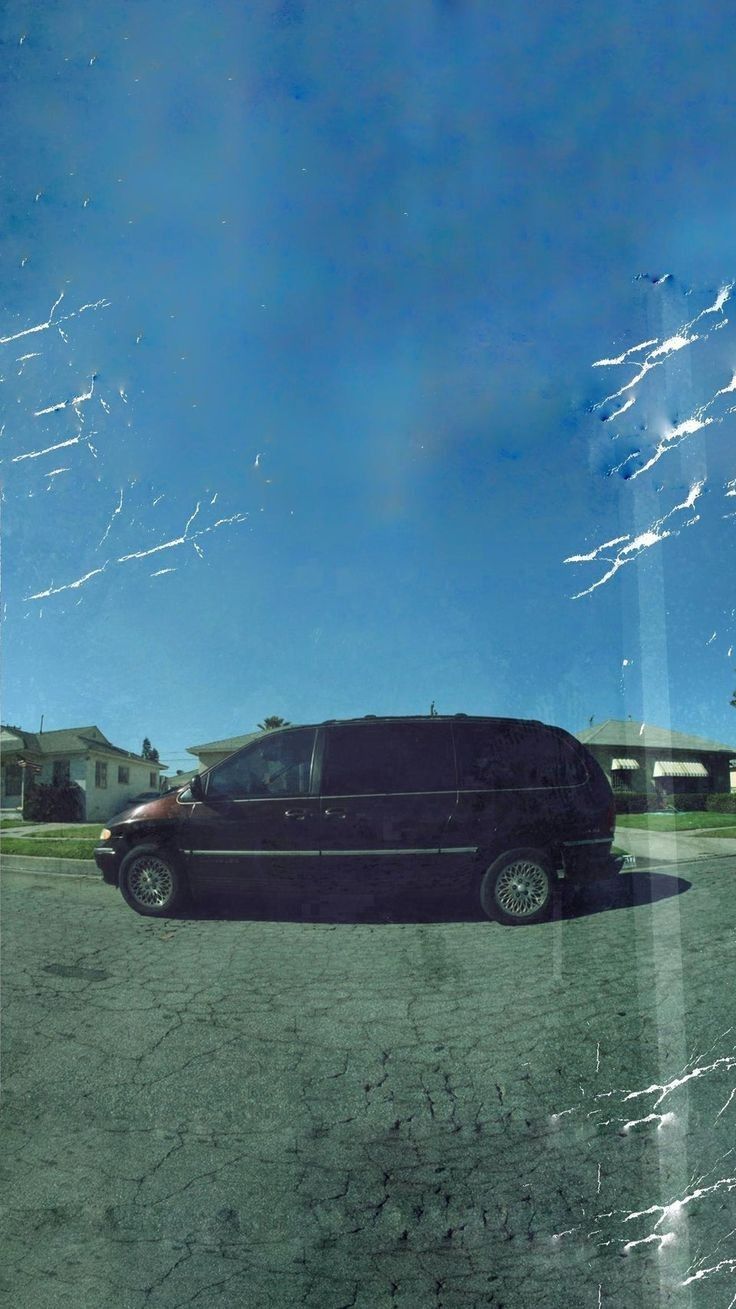 a black van parked in a parking lot next to some houses and grass on a sunny day