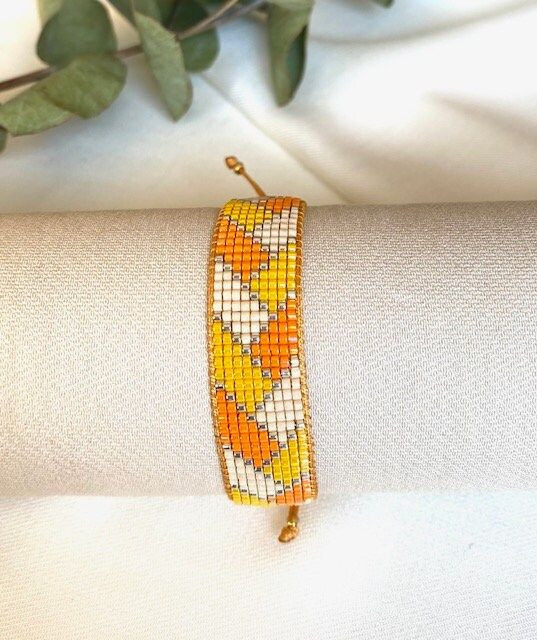 an orange and yellow beaded bracelet sitting on top of a white cloth next to a plant