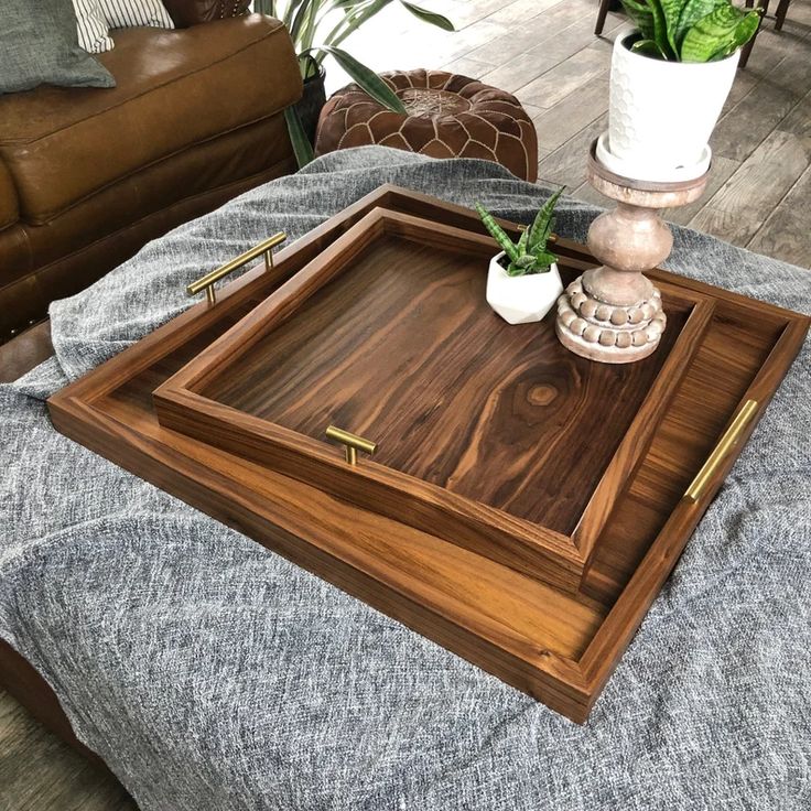 a wooden tray sitting on top of a couch next to a potted plant in a vase