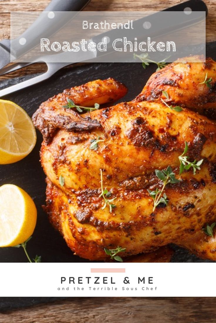 roasted chicken with herbs and lemons on a black platter next to a knife