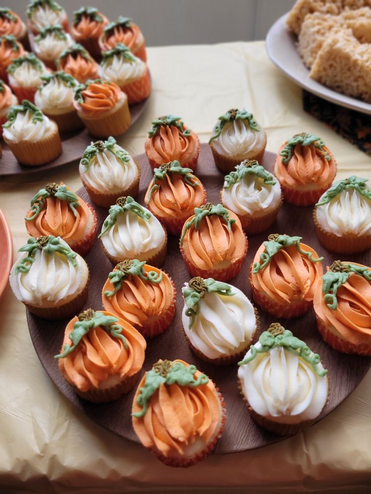 many cupcakes are arranged on a table with orange and white frosted icing