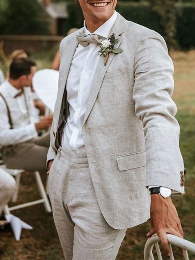 a man in a gray suit and bow tie smiles at the camera while others sit on lawn chairs