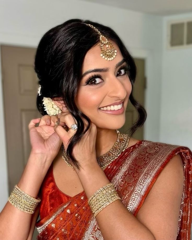 a woman in an orange and gold sari smiles at the camera while holding onto her jewelry